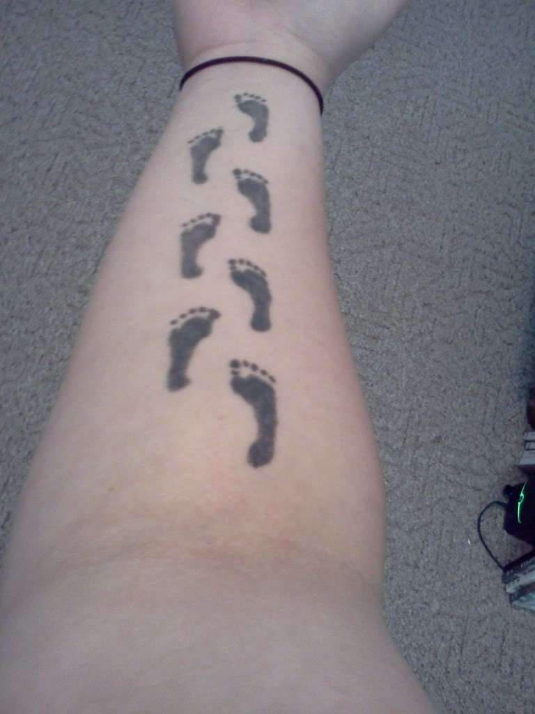 Black Ink Footprints Tattoo On Forearm