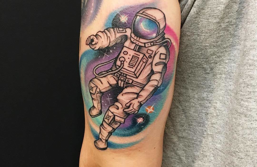 Black and colored astronaut with universe tattoo on upper sleeve