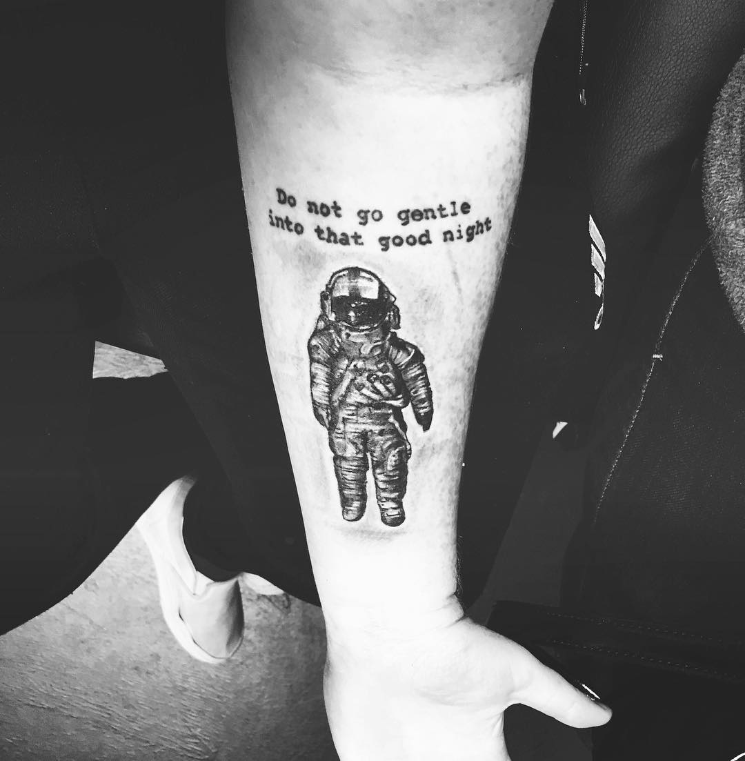 Black shaded astronaut with message tattoo on forearm