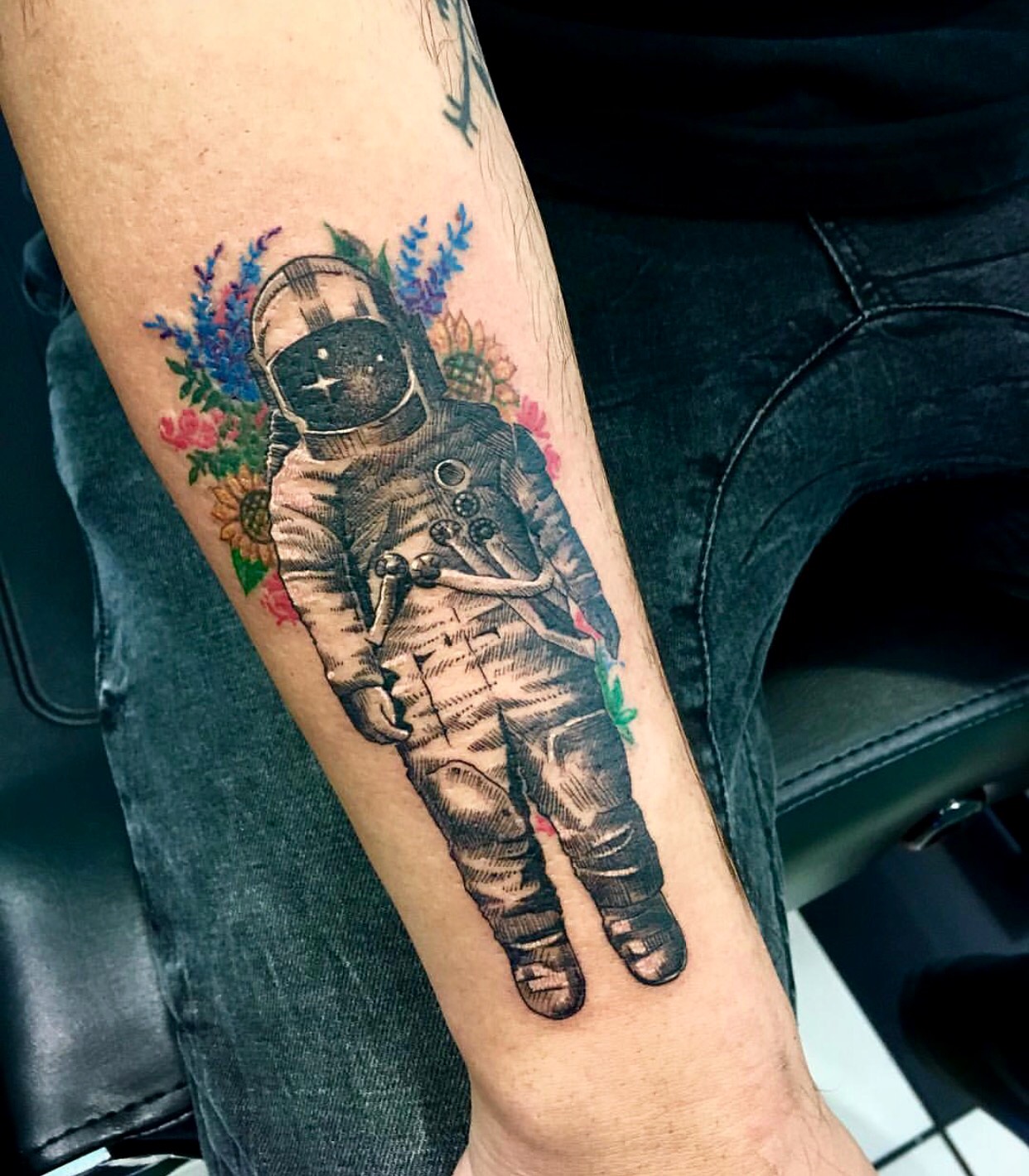 Grey shaded astronaut with colored flowers tattoo on lower arm