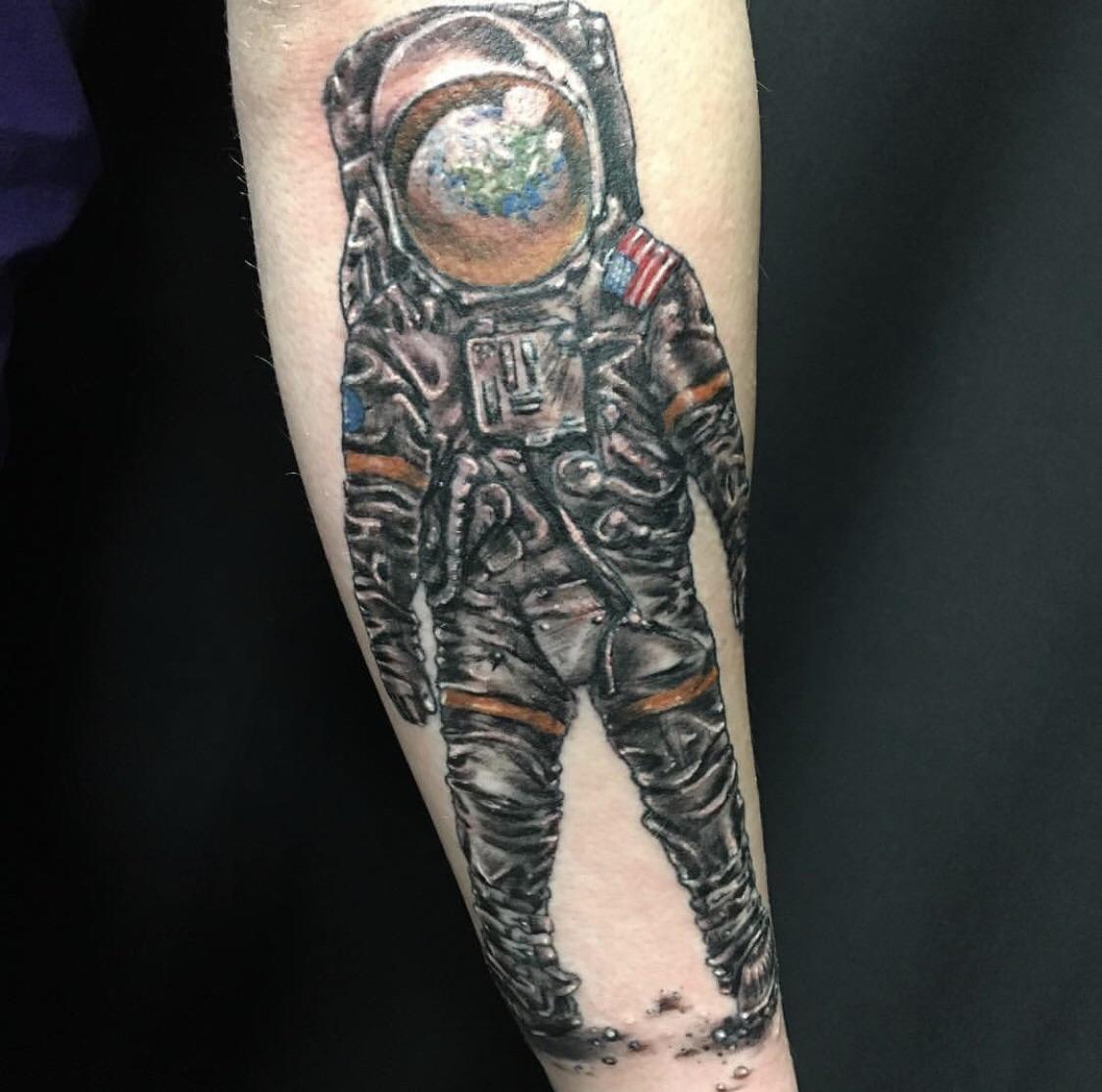 Grey shaded astronaut with earth face tattoo on inner forearm