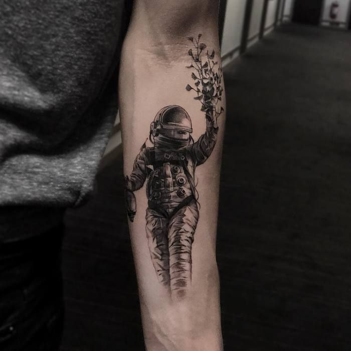 Grey shaded astronaut with plants tattoo on inner forearm